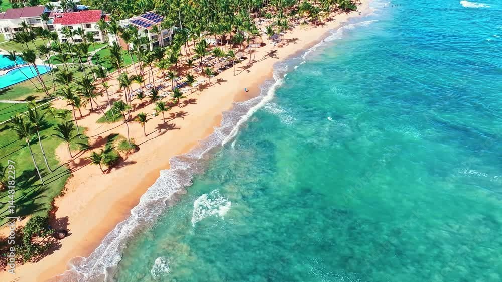 Drone view of tropical palm beach with yellow sand and turquoise waves. Perfect landscape background for summer vacation in Dominican Republic. Beach vacation concept on a sunny day. Drone view of tropical palm beach with yellow sand and turquoise waves. Perfect landscape background for summer vacation in Dominican Republic. Beach vacation concept on a sunny day.