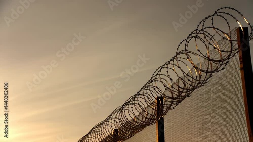 Security fence with razor wire silhouetted against a golden sunset

