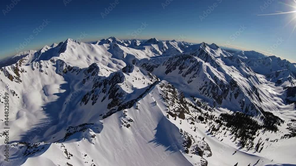 Aerial View of snow covered mountain. Drone flying over mountain ridge, snowy rock texture sun light blue sky landscape on winter Aerial View of snow covered mountain. Drone flying over mountain ridge, snowy rock texture sun light blue sky landscape on winter