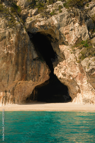 Turquoise water laps gently on the sandy beach of cala luna, with its iconic caves carved into the cliffs in sardinia, italy