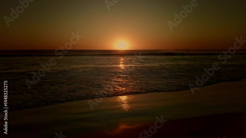 Sunset paints the beach with golden hues as silhouettes of people and children play in the ocean waves. Evening tranquility