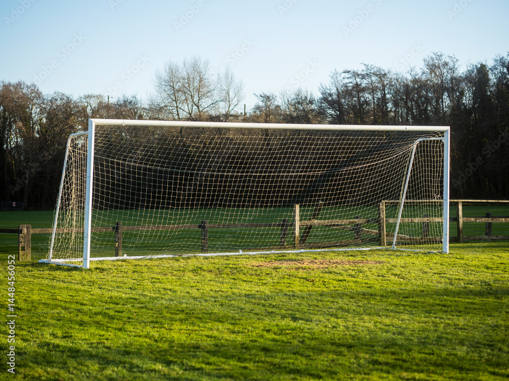 A soccer field with a goal and a fence in the background. The sky is cloudy and the grass is green. Football training ground. Popular outdoor sport. Nobody.