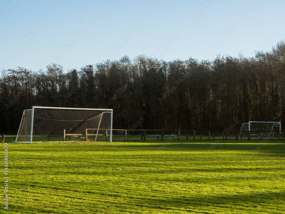A soccer field with a goal and a fence in the background. The sky is cloudy and the grass is green. Football training ground. Popular outdoor sport. Nobody.