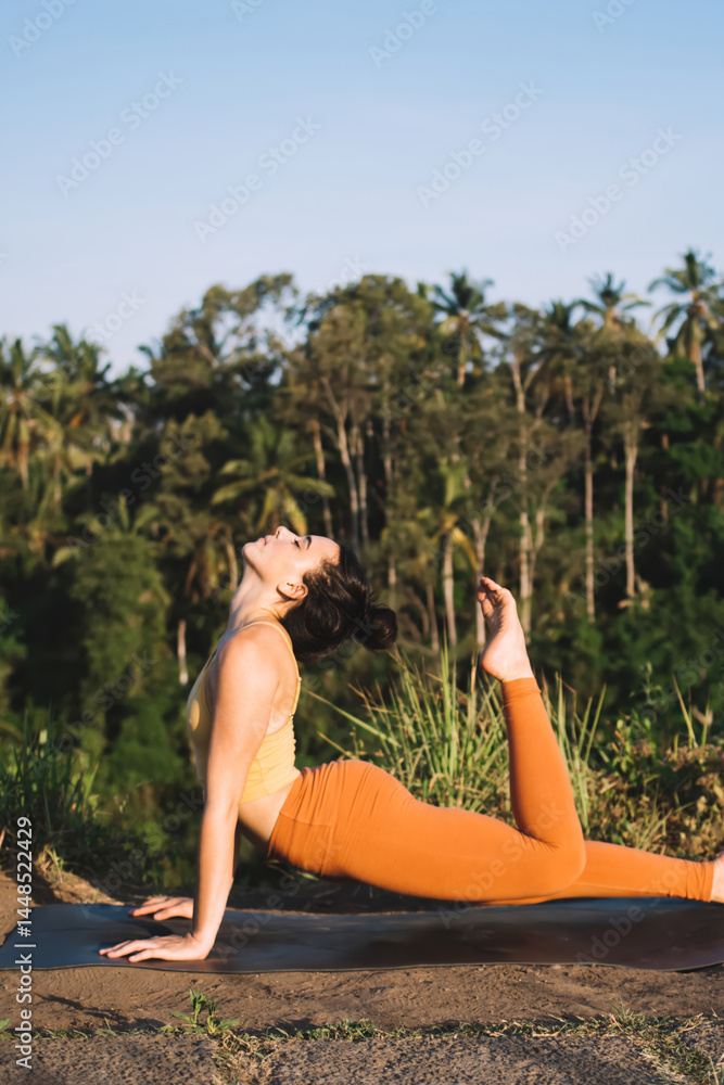 Flexible woman doing stretching asana while practicing yoga in nature
