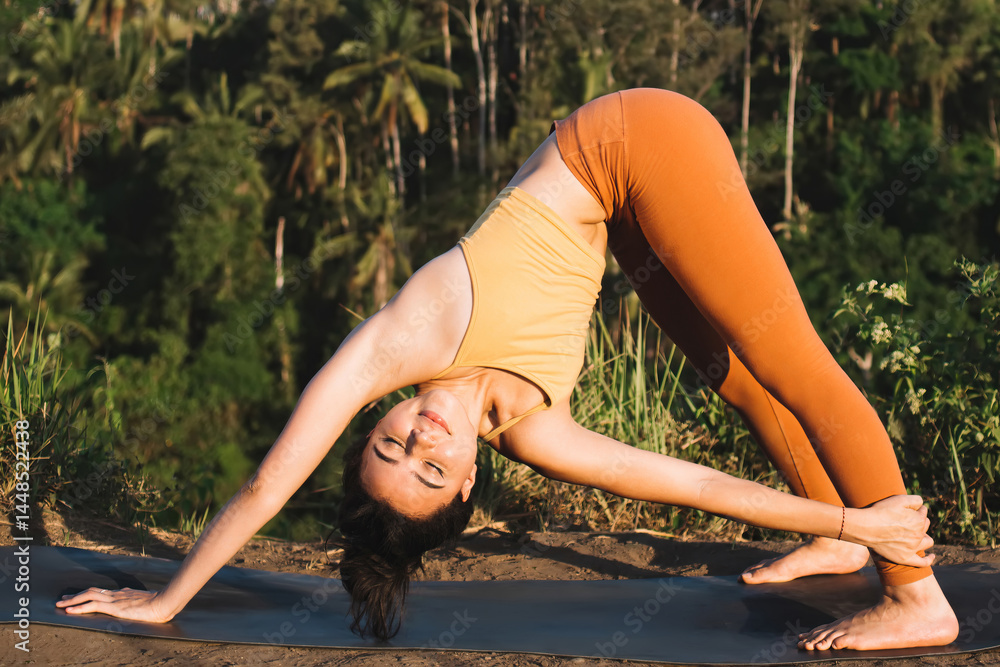 Strong caml female in activewear enjoying stretching and feeling body standing in asana on field in morning, tranquil caucasian woman enjoying yoga practice relaxing and keeping spiritual harmony