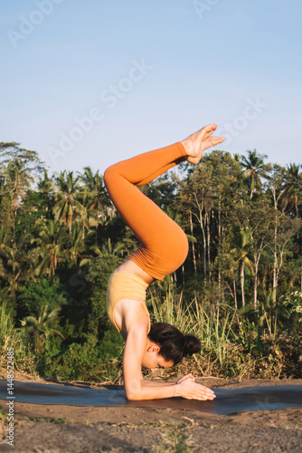 Obraz na płótnie Strong caucasian female in active wear standing in inverse asana on hands enjoying harmony and balance, calm concentrated woman feeling body during yoga practicing on field in morning w salonie