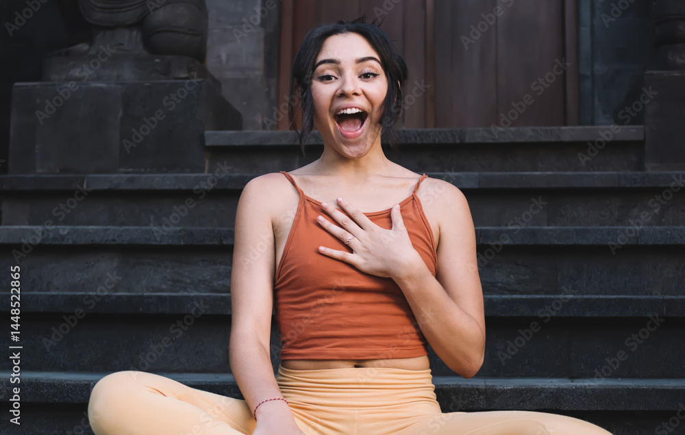 Portrait of expressive caucasian female in active wear enjoying free time and practice surprised with something, funny teen cheerful woman sitting in lotus pose smiling and looking at camera