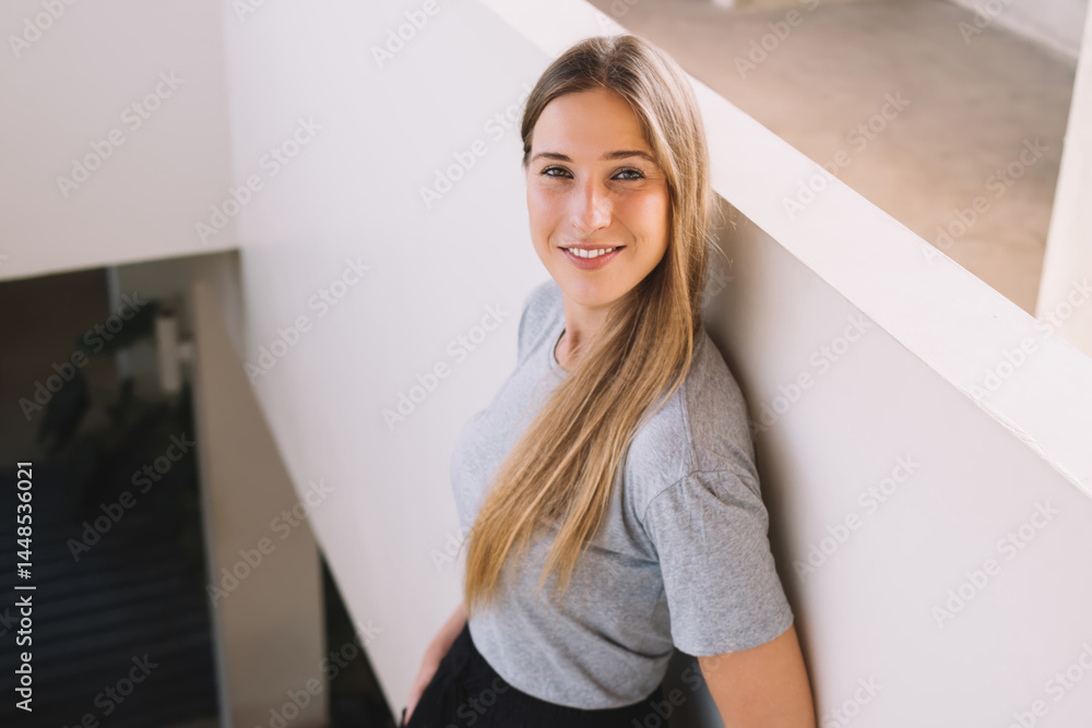 Smiling lady leaning on wall on stairs inside modern building