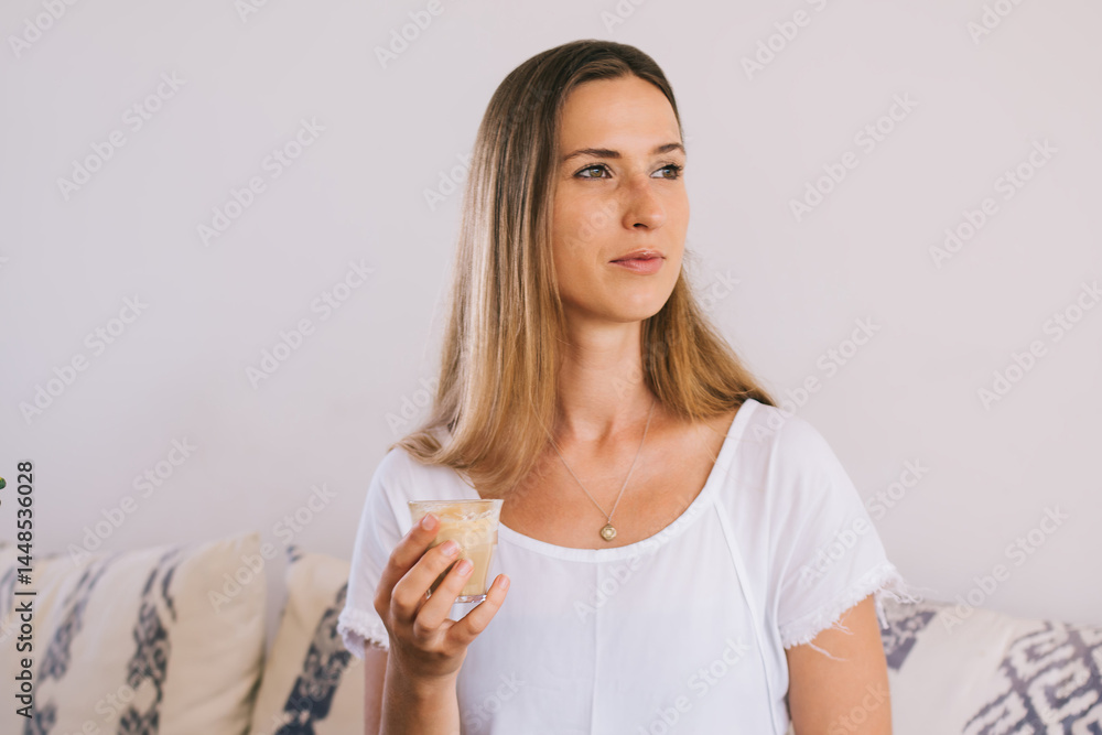 Female in summer outfit enjoying cold drink sitting on sofa