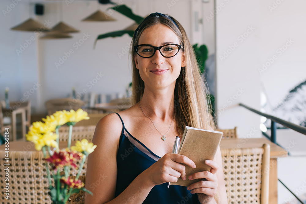 Cheerful woman with book in hands sitting in cafe