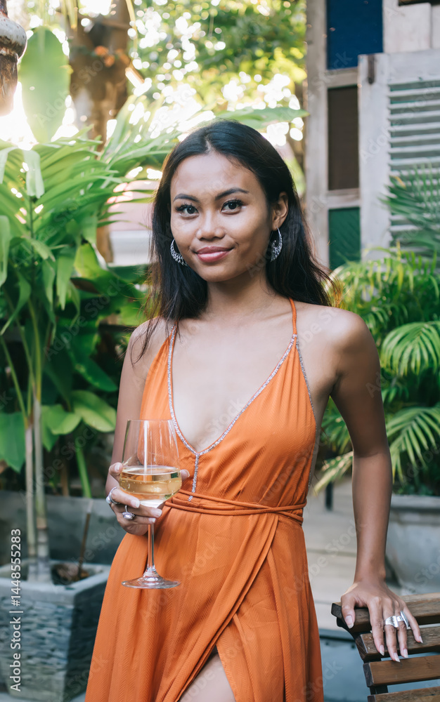 Smiling young ethnic woman with wineglass in tropical restaurant