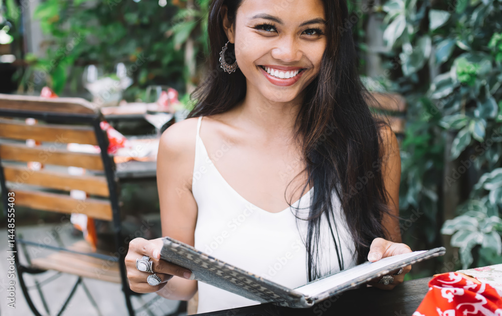Cheerful young woman reading menu in outdoor cafe