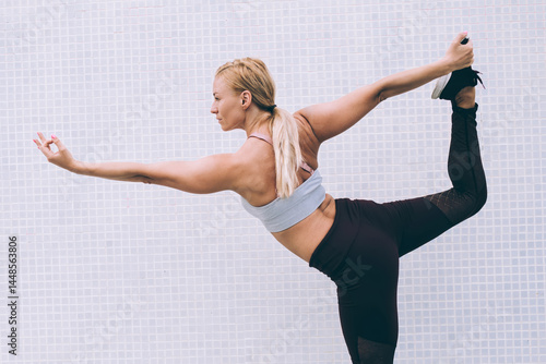 Obraz na płótnie Energetic slim woman in tracksuit doing Warrior one during yoga exercises in morning, female gymnastic enjoying virabhadrasana during time for physical recreation at publicity area with copy space w salonie