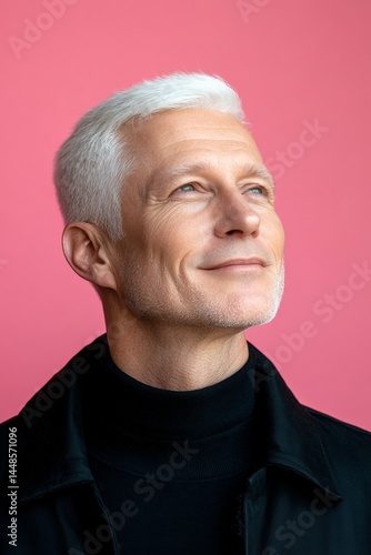 Idea of style for aging men. A happy man in a studio photo. Elegant men's ivy league haircut - midlife white man with white hair. A trendy and poised male showing charm. Pink solid backgrou.