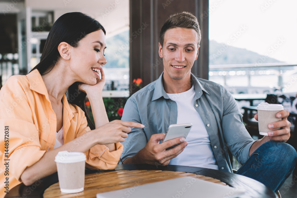 Young couple of smiling colleagues using smartphone in cafe