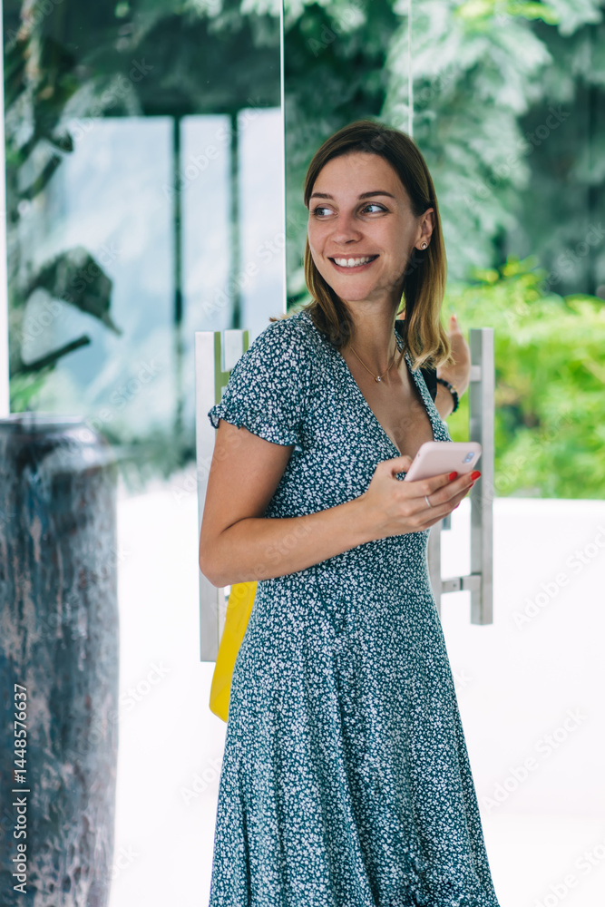 Cheerful millennial caucasian woman in casual wear entering smart home via mobile phone application, happy hipster girl open glass door using smartphone satisfied with modern technologies and gadgets