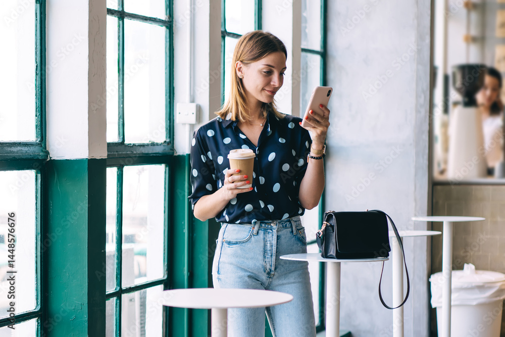 Smiling woman with cup of coffee using phone