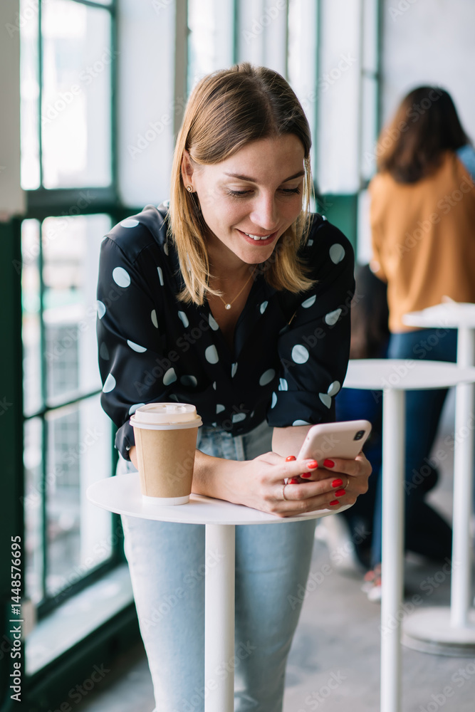 Positive blonde woman chatting and sending text messages on modern mobile phone connected to 4G, smiling female, young prosperous female blogger satisfied with sharing media on coffee break