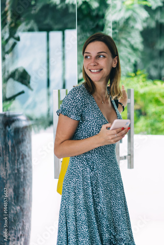 Cheerful millennial caucasian woman in casual wear entering smart home via mobile phone application, happy hipster girl open glass door using smartphone satisfied with modern technologies and gadgets