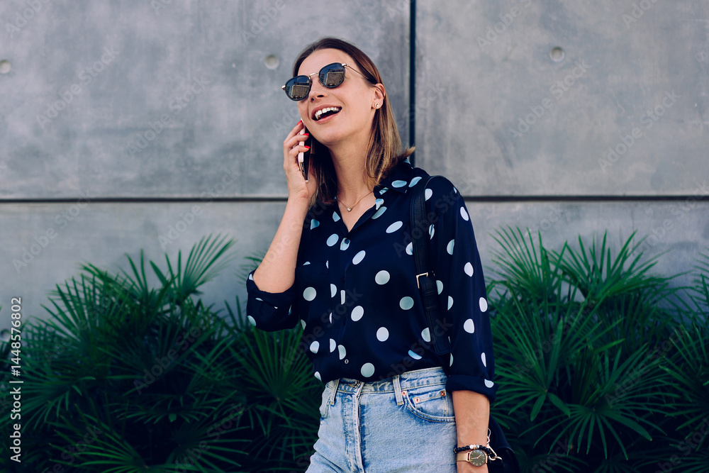Happy prosperous blonde woman in sunglasses and trendy wear having mobile phone talk carrying shopping bags, smiling hipster girl making smartphone call enjoying sales and discounts for buying