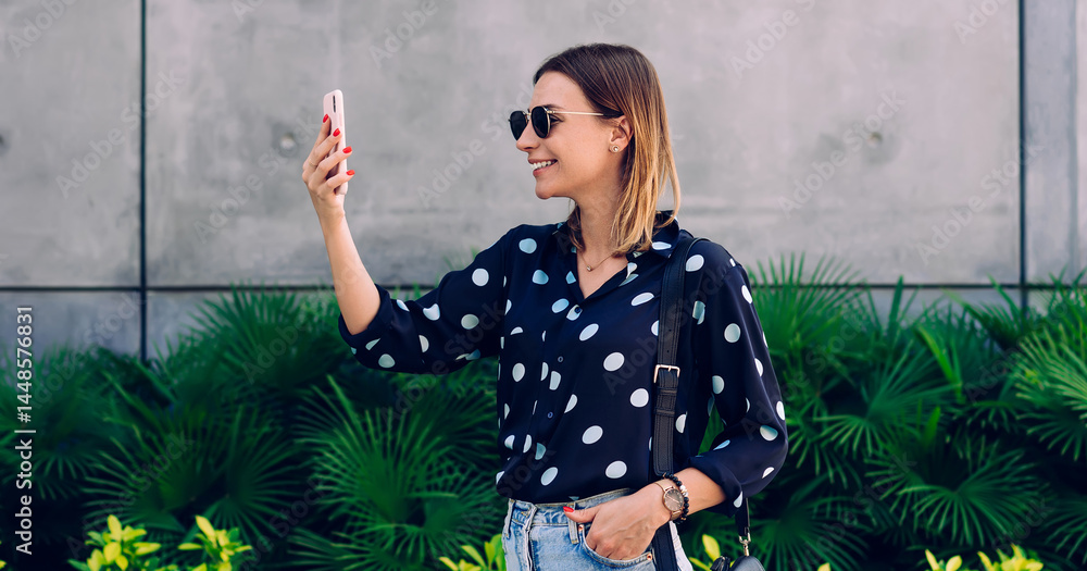 Young lady making selfie photo on smartphone while standing against stone wall