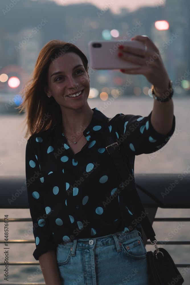 Smiling woman taking selfie against cityscape on embankment