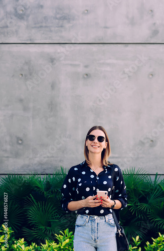 Positive young woman in sunglasses with smartphone on city street