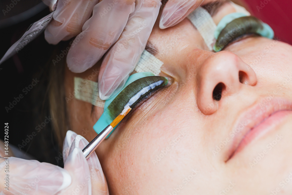 Eyelash lamination procedure on a woman's face. A cosmetologist glues long eyelashes with tweezers onto a woman's eye during an eyelash extension procedure.