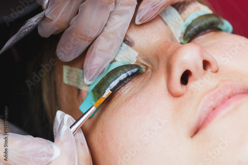 Obraz na płótnie Eyelash lamination procedure on a woman's face. A cosmetologist glues long eyelashes with tweezers onto a woman's eye during an eyelash extension procedure. w salonie