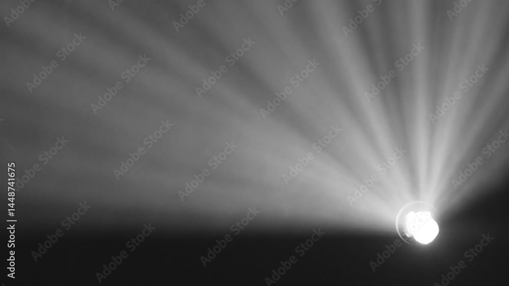 Bright blue spotlight projecting rays through haze or smoke, creating dramatic beams of light spreading outward in a dark environment with copy space.