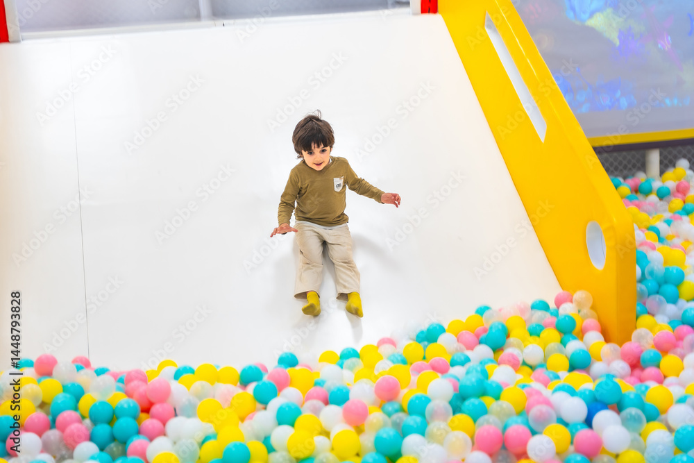 Happy child sliding into ball pit at indoor playground