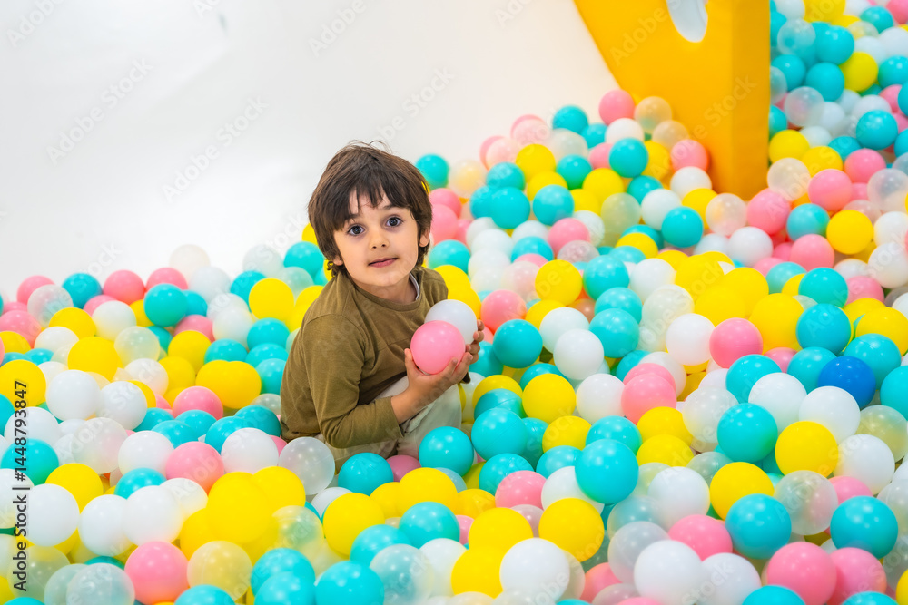 Happy child playing with colorful plastic balls in indoor playground