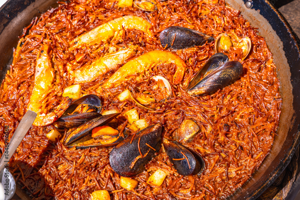 Fideua with prawns, mussels and clams cooking in a paella pan