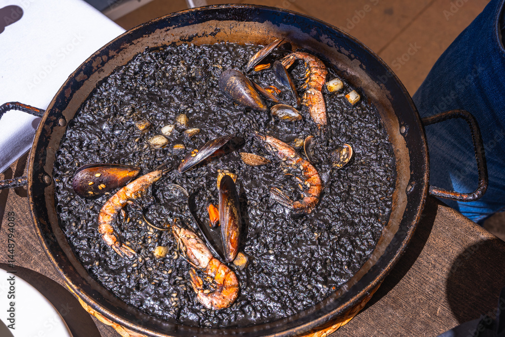 Paella negra with shrimps and mussels served in a pan