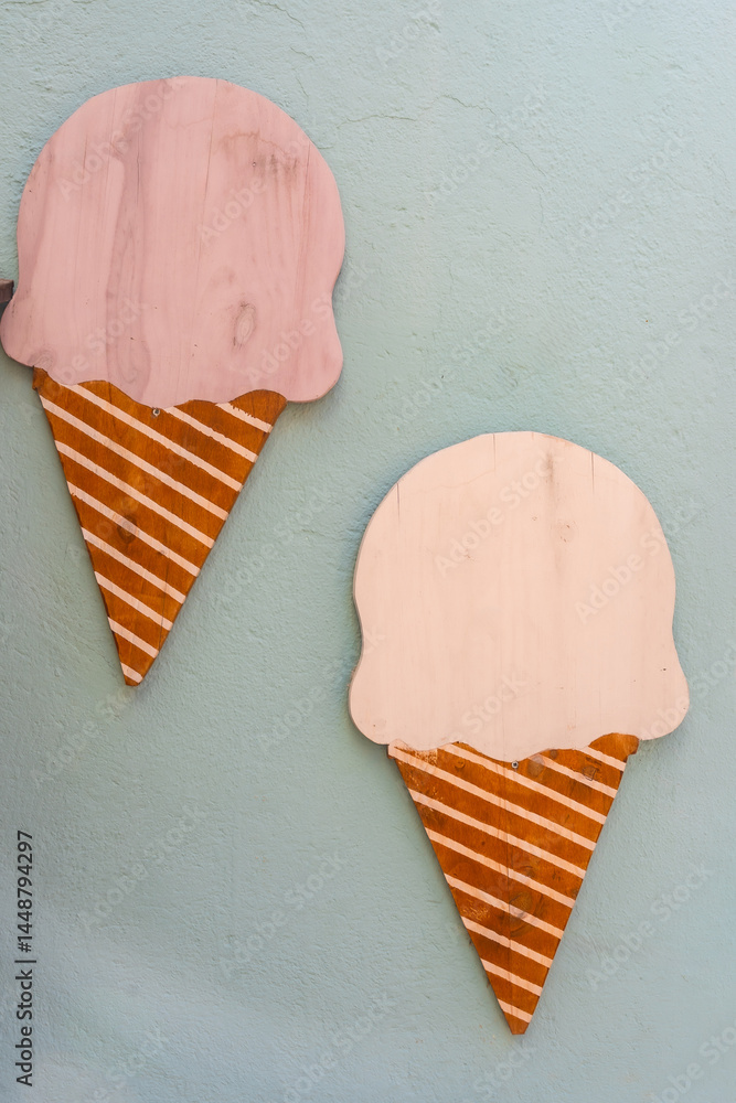 Two decorative wooden ice cream cones hanging on a light blue wall