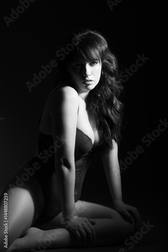 Studio portrait of a 30-year-old Canadian caucasian woman in a lace bodysuit, sitting on the ground. Split lighting creates a dramatic, moody, and sultry atmosphere with lingerie styling.