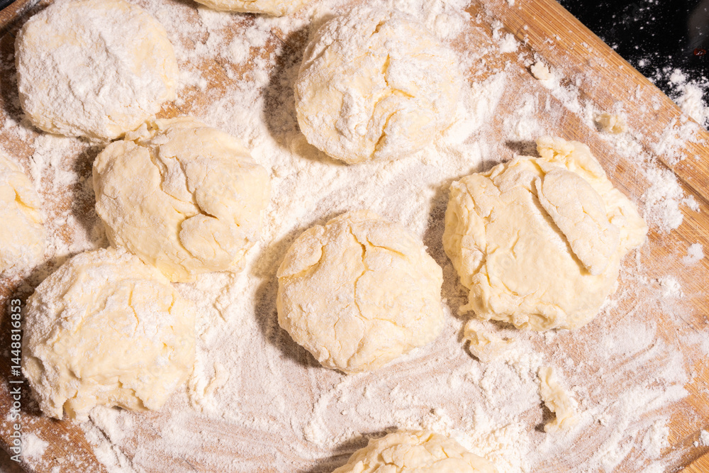 Several round dough balls rest on a wooden surface dusted with flour, prepared for baking.