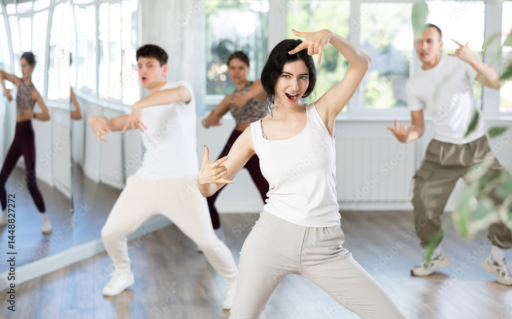 Fototapeta premium Happy enthusiastic young girl honing hip-hop moves in modern dance studio setting with group of women and men