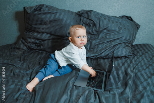 Obraz na płótnie Little boy toddler using laptop watching video at home, early education and learning. Little child looking at laptop screen and listening to music while sitting on bed. w salonie