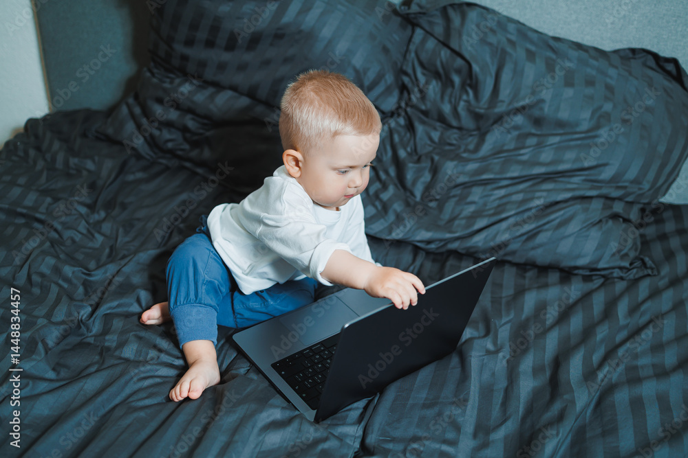 Cute little boy 2 years old sitting at home using laptop. Toddler boy watching video on laptop. Modern digitalization of children. Child watching educational videos on laptop.