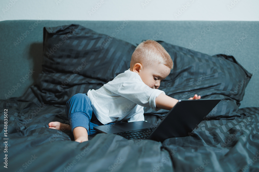 Cute little boy 2 years old sitting at home using laptop. Toddler boy watching video on laptop. Modern digitalization of children. Child watching educational videos on laptop.