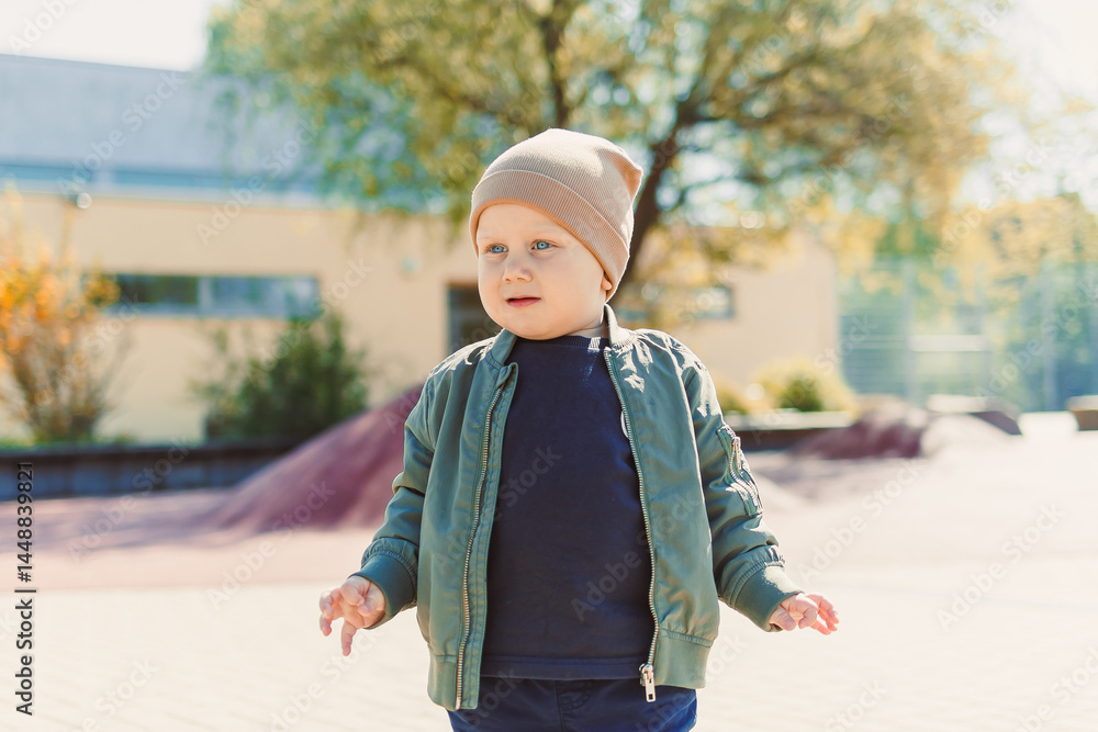 A 2 year old boy in a hat and jacket runs and plays outside. Toddler on a spring walk in the park. Child outdoors on a playground.