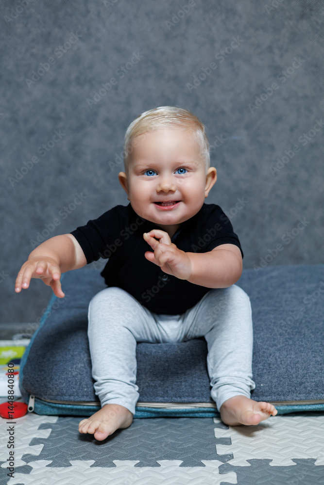 Blue-eyed blond boy 2 years old playing at home in the room. Toddler boy smiling looking at the camera. Home clothes for children.