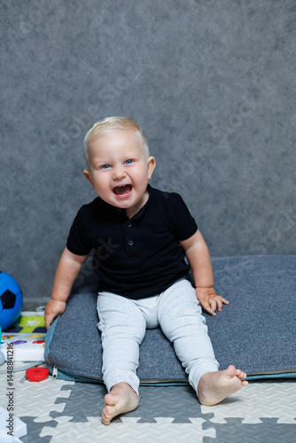 Obraz na płótnie Blue-eyed blond boy 2 years old playing at home in the room. Toddler boy smiling looking at the camera. Home clothes for children. w salonie