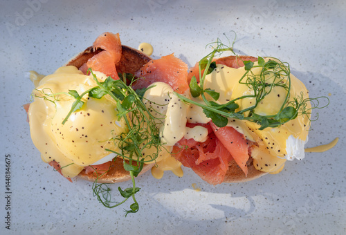 Obraz na płótnie Top view of Eggs Royale made with english muffin, oak smoked salmon, a brace of poached hen's eggs & hollandaise sauce and watercress served on blue ceramic tray. use it as your Wallpaper, Poster. w salonie