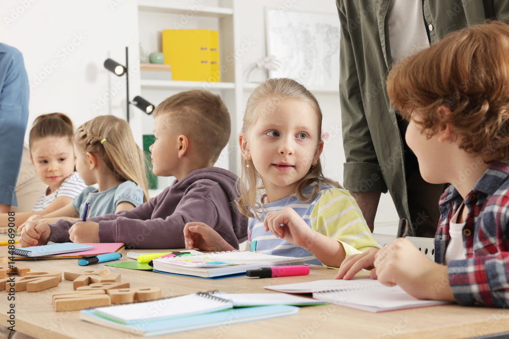 Children having lesson with teacher at desk indoors Children having lesson with teacher at desk indoors