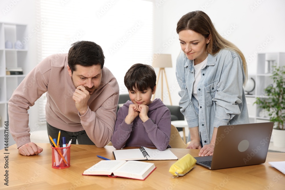 Parents helping their son with homework at wooden table indoors Parents helping their son with homework at wooden table indoors
