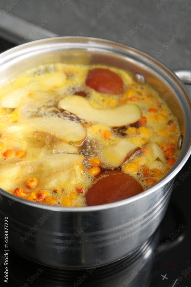 Making compot of apples and sea buckthorn berries. Simmering fruits in pot on stove, closeup Making compot of apples and sea buckthorn berries. Simmering fruits in pot on stove, closeup
