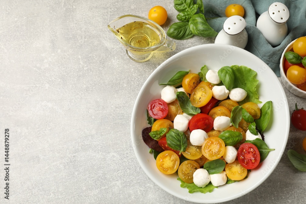 Tasty salad with yellow tomatoes, basil and mozzarella cheese on light grey table, flat lay. Space for text Tasty salad with yellow tomatoes, basil and mozzarella cheese on light grey table, flat lay. Space for text