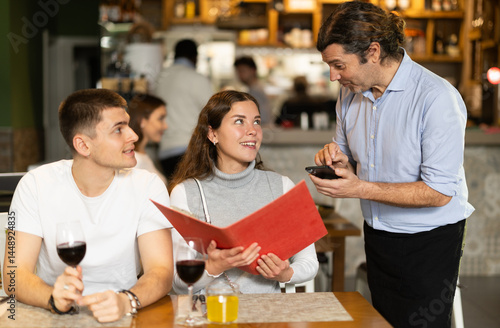 Obraz na płótnie Couple came to the restaurant for the anniversary, they drink wine and consult with the waiter about the choice of food. Man and a woman ordering from a waiter in a European restaurant in winter w salonie